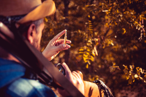 Hunting cartridge. Vintage Texas ranger with cartridge. Man is charging a hunting rifle. Hunter with shotgun gun on hunt. Cartridge case.