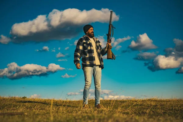 Hombre cazador barbudo sosteniendo arma y caminando en el bosque. Hunter con escopeta a la caza . — Foto de Stock