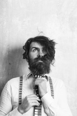 Uzun sakal ve bıyık yüzünde olan adam. Adam ya da işadamı dokulu duvar. İş moda ve güzellik. Moda şık saç modeliyle. Hipster gömlek ve pantolon askısı ile müzikal kravat.