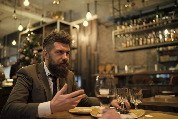 Bearded man in restaurant with companion. Business on go and communication. Confident bar customer speak in cafe. Date or business meeting of hipster in pub. Businessman with long beard in cigar club.