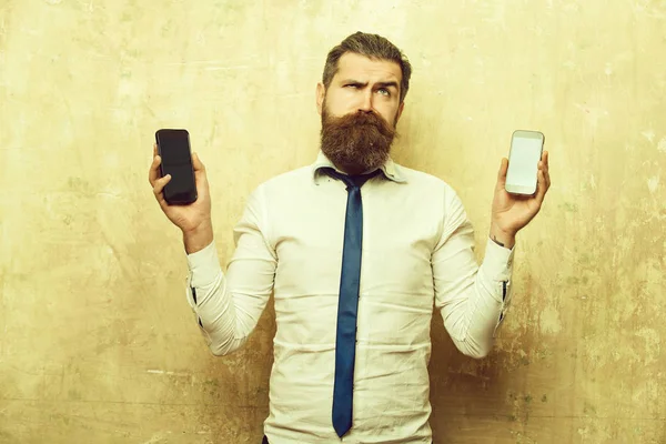 Hipster of bebaarde man vergelijk GSM en smartphone — Stockfoto