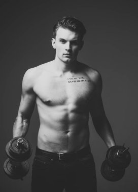 Kavram işe. Gövde, altı paketleri ile kas maço adam dambıl, koyu arka plan tutar. Dövme çekici adamla. Maço kas şekil, sporcu, vücut geliştirmeci ile kendine güvenen yüzünde.