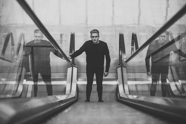 Young man with pensive face stands on escalator and raises