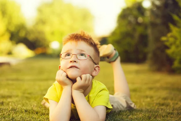 Babyjongen met rood haar in glazen op gras — Stockfoto