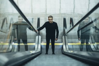 Genç adam dalgın yüzü ile yürüyen merdiven ve yükseltir üzerinde duruyor