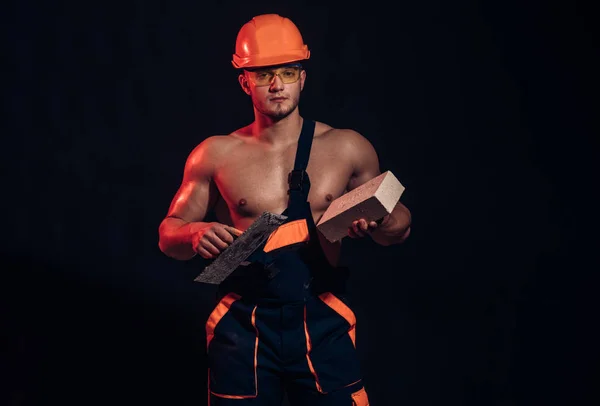 Our reputation is as solid as concrete. Muscular man does masonry work. Bricklayer worker. Construction worker or builder at work at building site. Man worker hold brick and trowel in muscular hands
