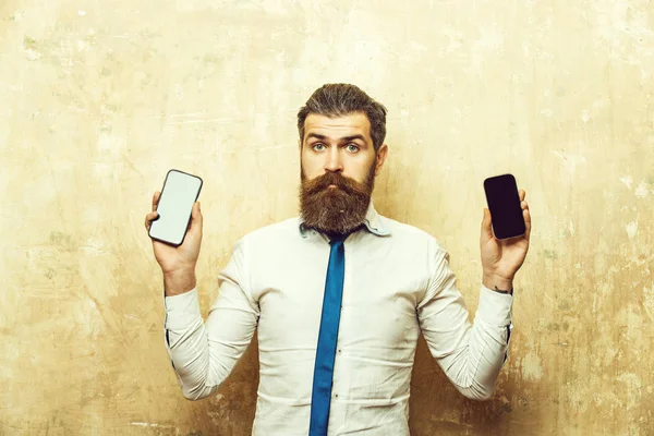 Hipster tai parrakas mies vertailla matkapuhelin ja älypuhelin — kuvapankkivalokuva