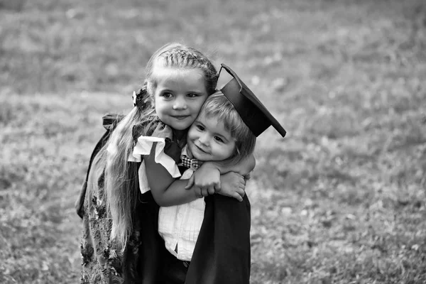 Cute girl hugging happy boy in graduation hat and robe — Stock Photo, Image