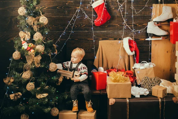 Criança bonito está decorando a árvore de Natal dentro de casa. O miúdo aproveita o feriado. Crianças de Natal - conceito de felicidade. Um miúdo engraçado a segurar um presente de Natal. Férias de celebração . — Fotografia de Stock