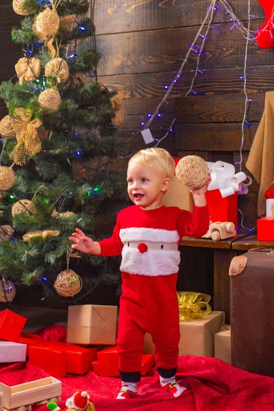 Eröffnungsgeschenke zu Weihnachten und Neujahr. glückliches Kind mit einem Weihnachtsgeschenk auf Holzuntergrund. Porträt Kind mit Geschenk auf Holzgrund. Christbaumschmuck. Kindergeschenk. — Stockfoto