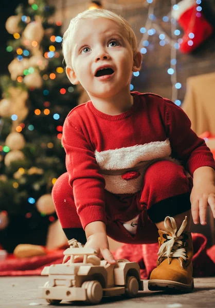 Freudiges Baby, das Weihnachten zu Hause in die Kamera schaut. Kindergeschenk. Kinder haben Spaß in der Nähe des Weihnachtsbaums drinnen. Frohe Weihnachten und ein gutes neues Jahr. Konzept für Weihnachtsgeschichte. — Stockfoto