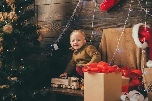 かわいい子女の子は、室内にクリスマス ツリーを飾っています。木製の背景に贈り物で子供の肖像画。新しい年の子供。クリスマス物語のコンセプト。幸せな子供. — ストック写真