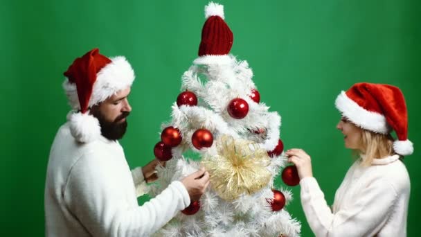 Homem e mulher em uma cabeça de anos novos decoram a árvore de Natal no contexto verde. Conceito de celebrar o ano novo e o Natal . — Vídeo de Stock