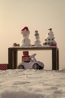 Kardan adam ve xmas baubles ile ağaç. Kar beyaz gökyüzü üzerinde ahşap masa üzerinde heykeller. Noel ve yeni yıl kutlama. Oyuncak araba karlı zemin üzerine mevcut kutuları ile. Kış tatil kavramı.