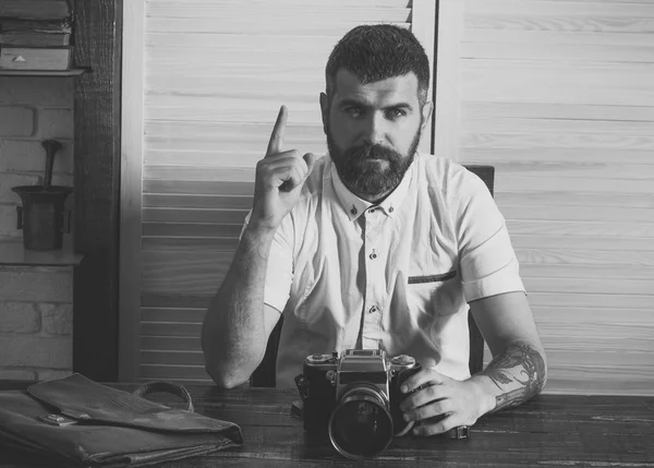 Bearded man with camera and raised finger up at desk
