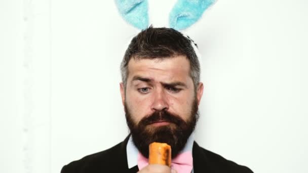 Bearded man wearing a suit and with ears of a rabbit eat carrots and shows different emotions. Funny man with rabbit ears. — Stock Video