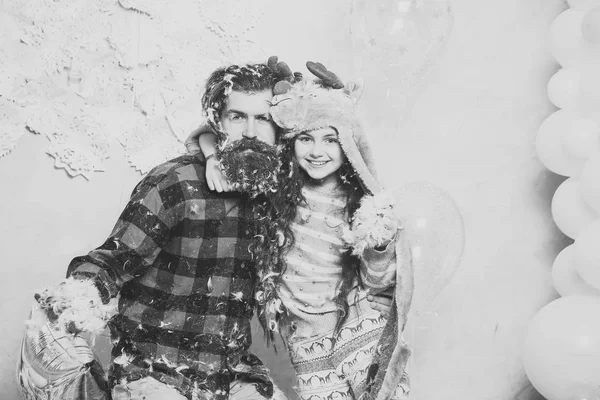 Frohe Weihnachten niedliches kleines Mädchen oder hübsches Kind mit Wintermütze und bärtigem Mann in kariertem Hemd mit Federn im Gesicht, in der Nähe silber-weißer Luftballons und dekorativer Neujahrsschneeflocken — Stockfoto