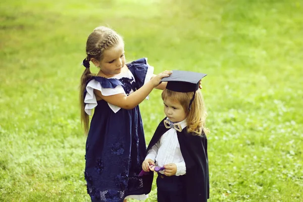 Ładna dziewczyna opatrunku mały chłopiec w graduacyjnej kapelusz i płaszcz — Zdjęcie stockowe