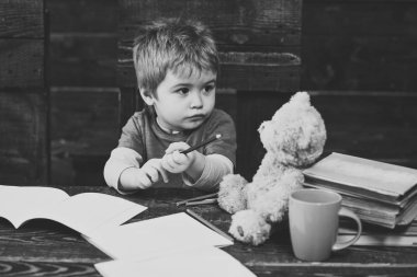 Okuldaki meşgul çocuk. Küçük çocuk copybooks ile tahta masada oturuyor. Sarışın çocuk onun oyuncak ayı arıyorsunuz