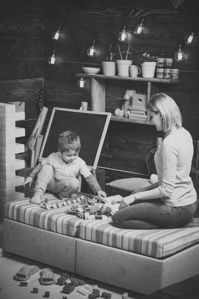 Mamma och barn leka med detaljer av konstruktören, plastklossar. Moderskap koncept. Plantskola med svarta tavlan på bakgrund. Mor och son spela med konstruktorn. Familj spelar med konstruktorn hemma. — Stockfoto