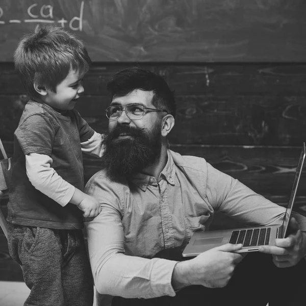 Papá sonriente enseñando a su hijo habilidades informáticas. Padre e hijo mirándose el uno al otro. Niño de pie abrazando a su padre sentado por el cuello —  Fotos de Stock