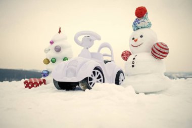 Kardan adam ve oyuncak araba karlı zemin üzerine. Gülen yüz kış gününde ile kar heykel. Noel ağacı ve beyaz gökyüzü mevcut kutusunda. Noel ve yeni yıl. Tatil kutlama kavramı.