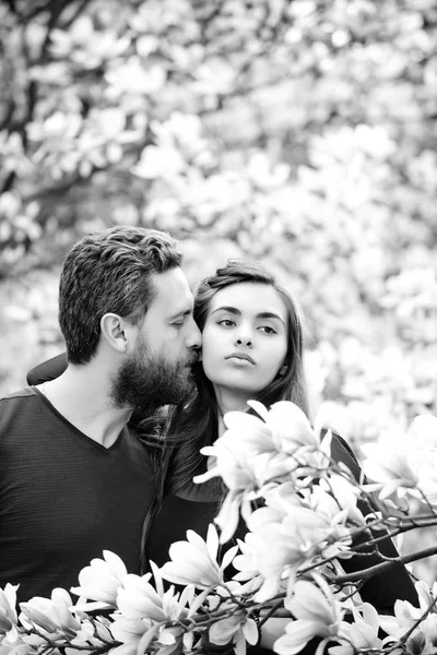 Мужчина целует красивую девушку на цветущих деревьях с магнолией — стоковое фото