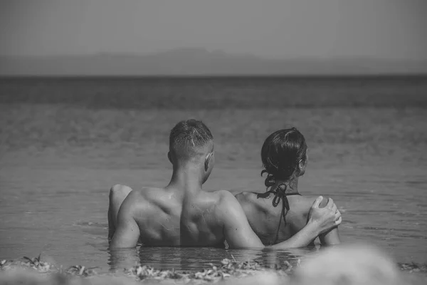 Couple in love relaxing on holiday, honeymoon. Happy couple relaxing, sun tanning on beach, lying in water, looking at ocean, copyspace. Honeymoon and vacation concept. Young lovers swim in sea. — Stock Photo, Image