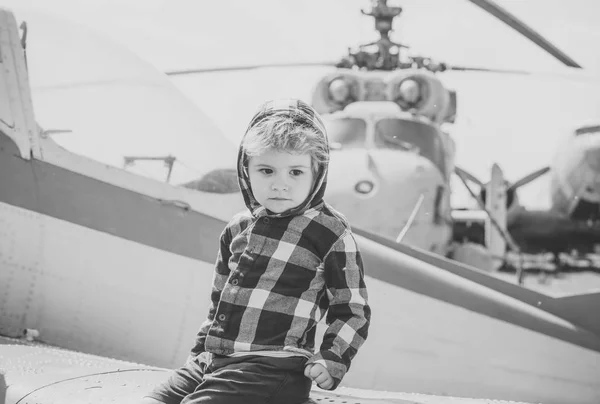Roztomilý chlapec sedí na křídle staré letadlo v leteckém muzeu. Texturou grunge starý vrtulník a obloha s mraky na pozadí. Kid na výlet do muzea letectví ve volné krajině. Vzdušné síly historie konceptu. — Stock fotografie