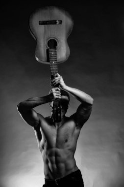 Genç yakışıklı adam kas vücut çıplak göğüs ve akustik gitar gri arka plan üzerinde tutarak Studio poz gövde