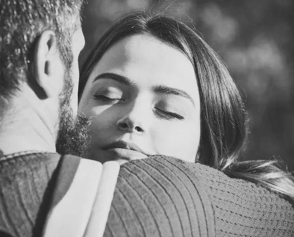 Couple in love hugs on green blurred background, autumn day. Couple with dreamy face cuddle each other with tenderness. Man with beard and young woman happy together. Love and romantic concept.