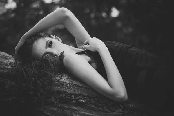 Frau mit langen brünetten Haaren entspannen auf Baum in der Natur. Frau mit lockiger Frisur im Sommer. Haarpflege, Therapie und Behandlung. Mädchen mit Make-up Gesicht, Schönheit. Mode-Model mit Glamour-Look — Stockfoto