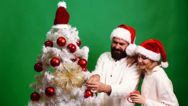 若いカップルは、緑の背景にクリスマス ツリーを飾っています。新しい年のお祝いのコンセプトです。幸せそうな顔で愛情のあるカップルはクリスマス ツリー近く新年を満たすため. — ストック動画