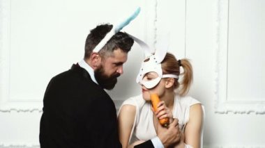 Adam bir kadın tarafından bir deri maske havuç besleme tavşan kulaklı sakallı. BDSM kavramı. Beyaz bir arka plan üzerinde tavşan kulaklı tutkulu çift.