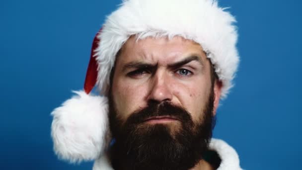 Крупный план бородатого человека в новогодней шляпе, который двигает бровями. Бородач двигает бровями на синем фоне. Концепция праздников . — стоковое видео