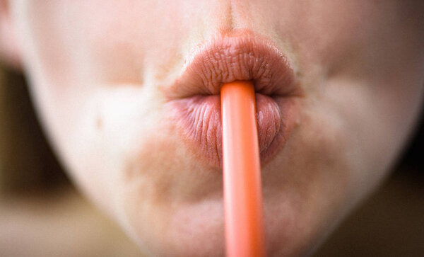 Drinking straw. Drinking straw in mouth. Sipping drink through straw. Female lips while drinking with straw. Drinking tube is a small pipe to consume a beverage. Orange plastic tube. In small sips.