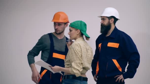 Three builders are discussing the construction plan. Concept of construction works. Woman and two men in helmets are considering a construction plan. — Stock Video