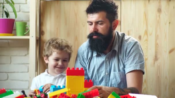 Padre e figlio stanno giocando con un designer di plastica. Un piccolo figlio viene giocato con suo padre. Famiglia e giocattoli, felice bel bambino e barbuto padre elegante . — Video Stock