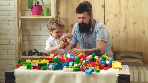 Familje-och barndoms koncept. Pappa och Kid bygga plast block. Far och son med glada ansikten skapa färgglada leksaker med färgade tegelstenar. Man och pojke leker tillsammans. — Stockvideo