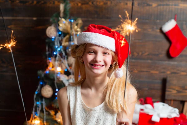 Happy little girl dressed in winter clothing think about Santa near Christmas tree. Smiling Little girl peeping from behind Christmas tree in living room.