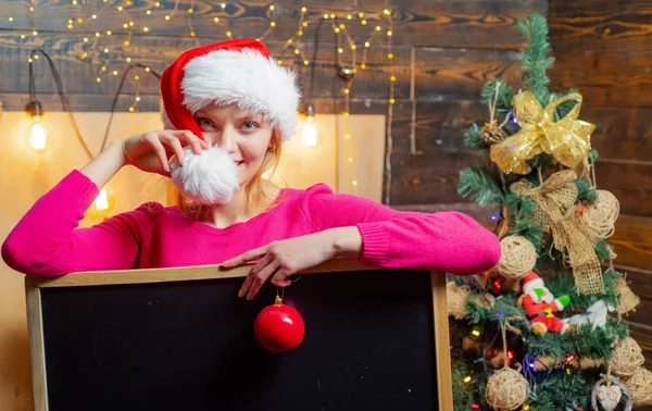 Femme de Noël tenant un bureau noir pour le texte. Espace de copie du tableau noir. Santa femme posant. Sexy Santa Clause femme en robe élégante. Noël et nouvelle année concept . — Photo