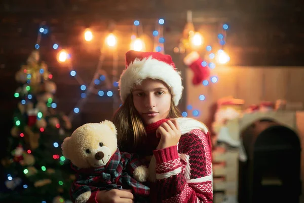 Christmas tonåring. Söt liten flicka Tonåring dekorera julgran inomhus. Lycklig liten flicka klädd i vinter kläder tycker om Santa nära julgran. — Stockfoto