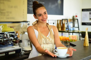 Bugünün iyi bir ruh hali kahve tarafından desteklenmektedir. Kadın barista kahve dükkanında. Barista gülümseme ile fincan sıcak kahve içecek hizmet. Güzel kadın stand Cafe tezgahın arkasındaki. Kafede kahve bira