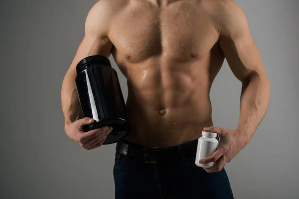Трансформация тела с помощью диеты. Анаболический гормон увеличивает мышечную силу. Сильный человек держит в руках витаминные бутылки. Человек с шестью кубиками пресса. Мышцы растут с анаболическими стероидами. Витаминное питание. Здоровое питание — стоковое фото