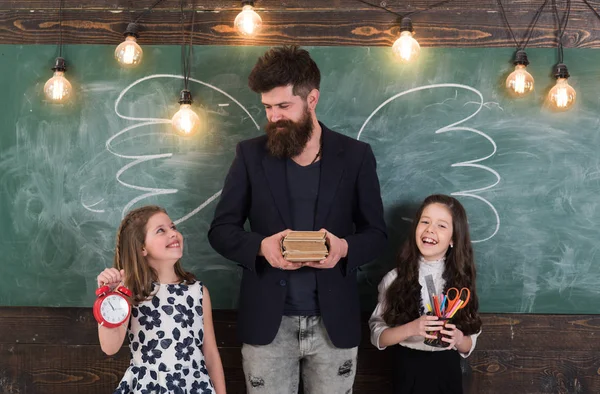 Favoritlärare koncept. Mannen med skägg och skolflickor med skolan attribut. Lärare och flickor elever i klassrummet, svarta tavlan på bakgrund. Barn och lärare med teckningar av krita vingar. — Stockfoto