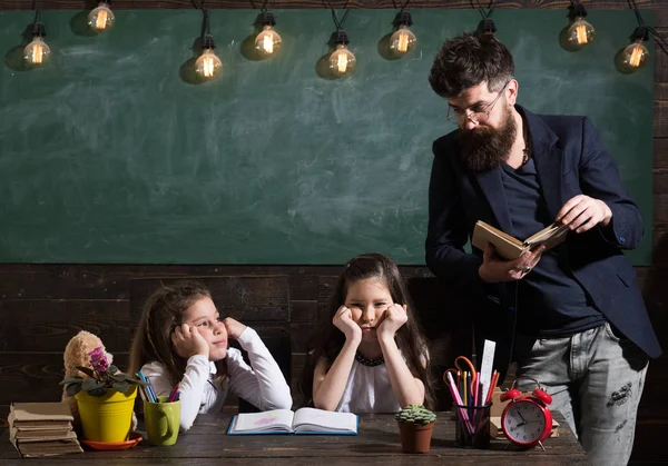 Άνδρας με γενειάδα διδάσκει μαθήτριες, διαβάζοντας το βιβλίο. Βαρεθεί και κουραστεί ακούγοντας δάσκαλος σε παιδιά. Δάσκαλος και τα κορίτσια τους μαθητές στην τάξη, chalkboard σε φόντο. Βαρετό μάθημα έννοια. — Φωτογραφία Αρχείου