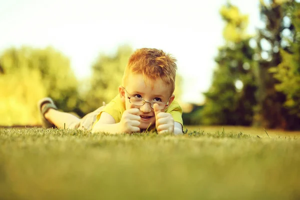 Niño feliz con el pelo rojo en gafas en la hierba —  Fotos de Stock