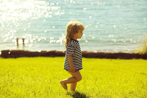 Cute baby boy in striped tshirt walks on green grass — Stock Photo, Image