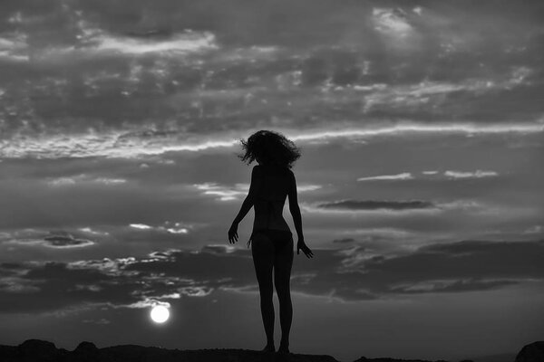 Young woman silhouette on beach near sea or ocean water in evening or twilight sunset summer day on natural background