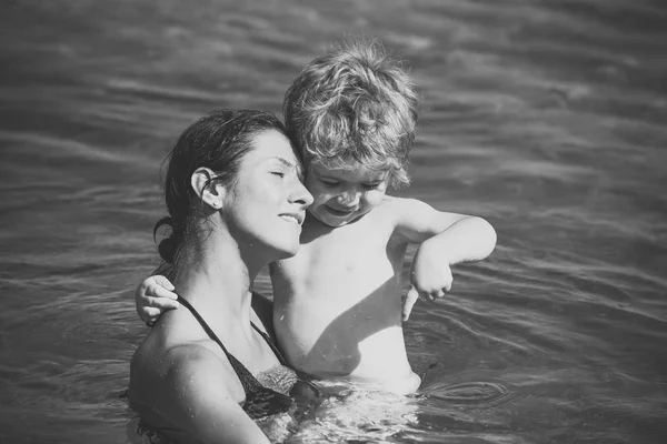 Niño lindo jugar con agua en el océano, el mar. Concepto de maternidad. Madre lleva al hijo en las manos, abraza al niño. Mamá y el niño con caras sonrientes pasan tiempo juntos en el mar en el día soleado . — Foto de Stock